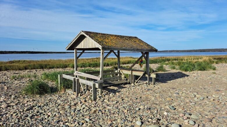 A small wooden structure sits on a rocky beach under a blue sky.