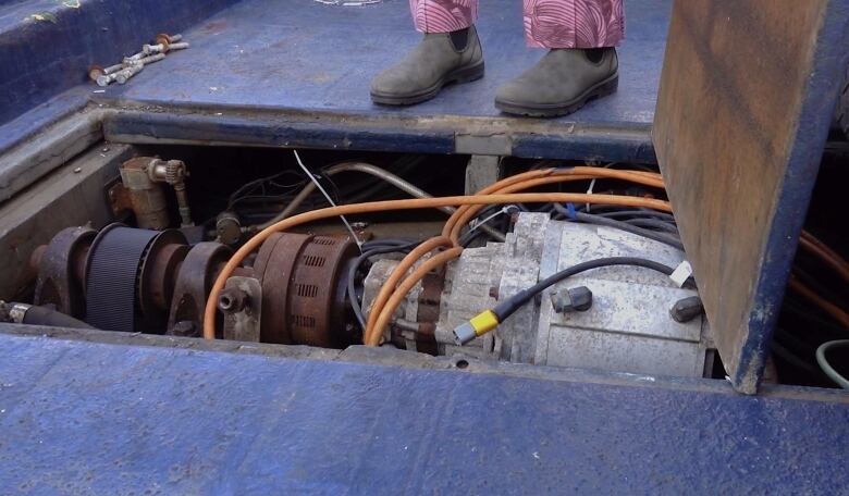 A metal driveshaft is seen though a floor panel on the boat deck.