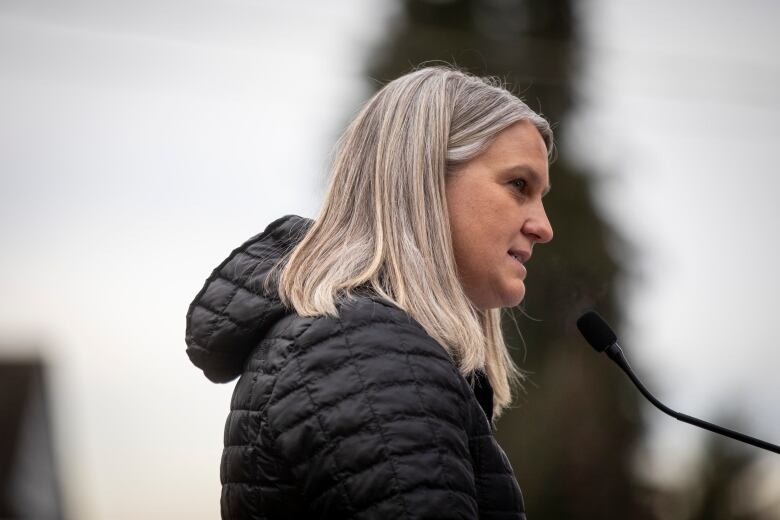 A woman with white-blonde hair is seen in profile as she talks into a mic.