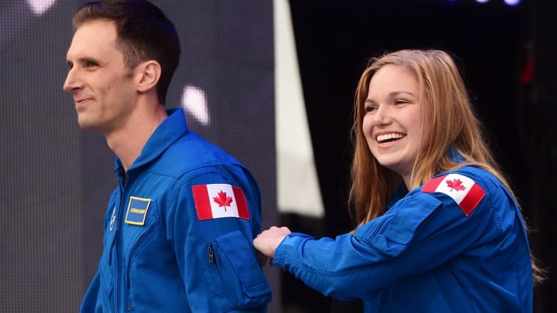 Joshua Kutryk and Jenni Gibbons are seen in their blue space jumpsuits, smiling.