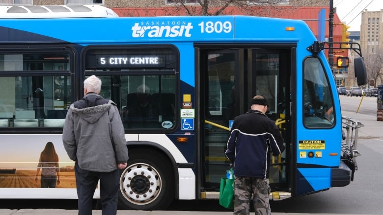 Two people stand with only their backs visible and a bus is stopped in front of them