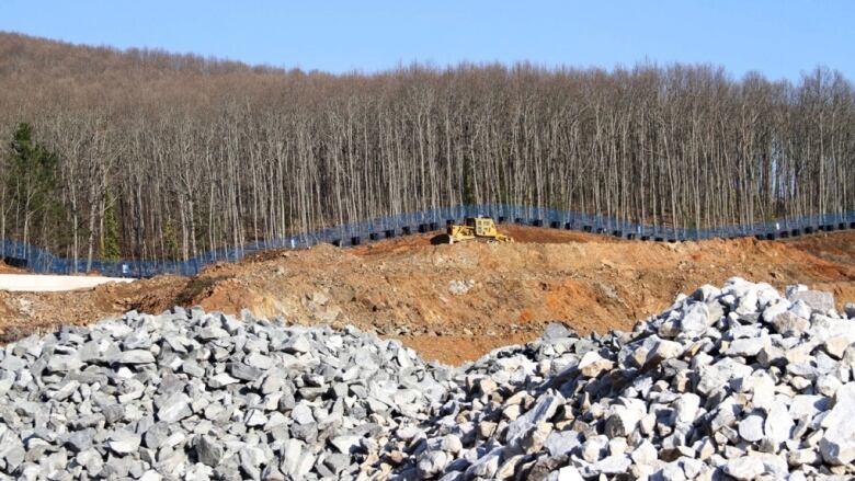 A big machinery rolls through ore with a line of trees in the background.