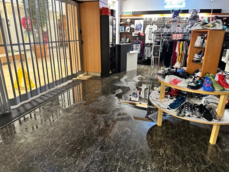 Water is shown on the floor of a store with colourful sneakers on tables of displays off the ground. 