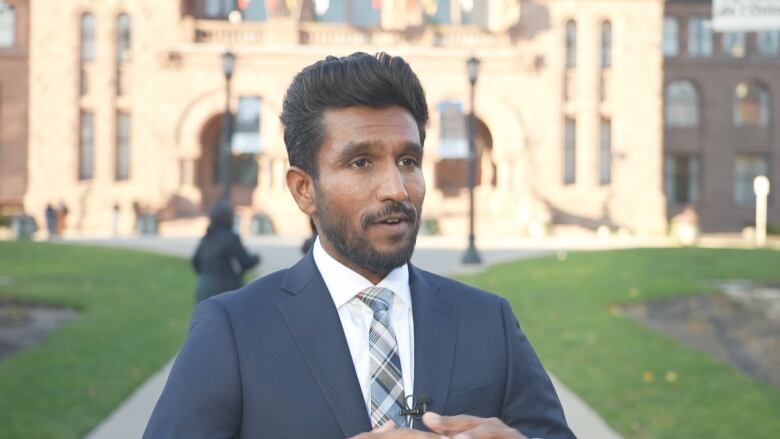 A bearded man in a suit stands outside Queens Park in Toronto on a cold, sunny day.