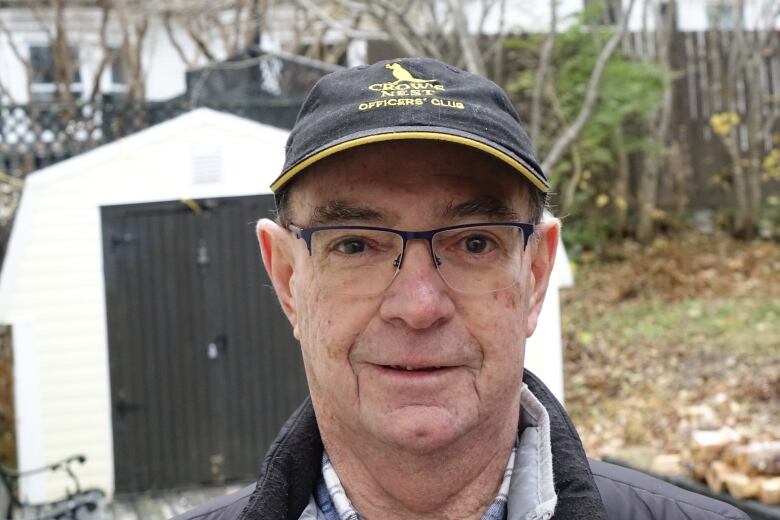 A man wearing a hat stands outside his home.