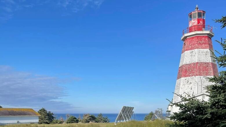 An octagonal red and white lighthouse with the ocean seen in the background.