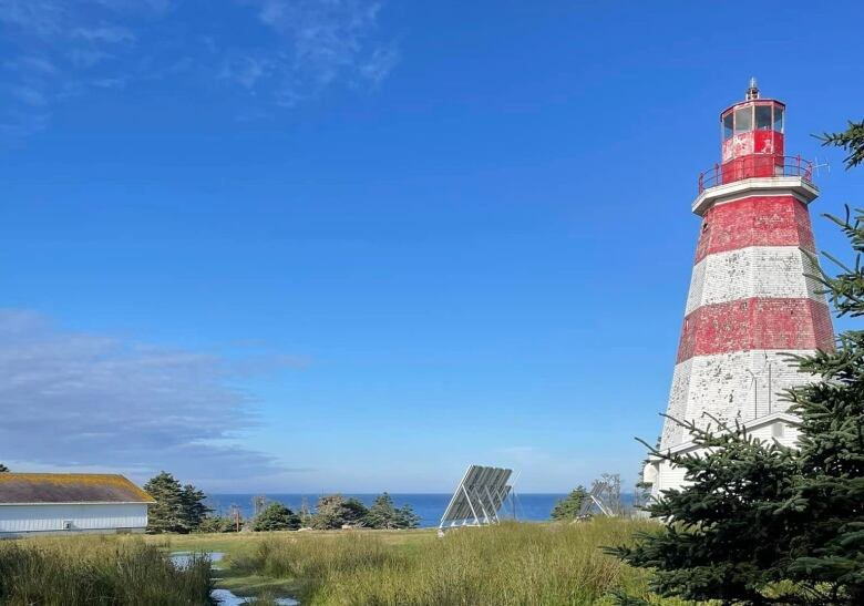 An octagonal red and white lighthouse with the ocean seen in the background.