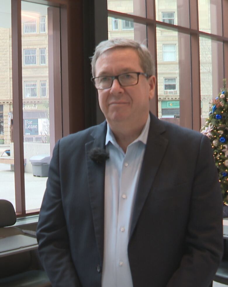 A man stands in a lobby, next to a Christmas tree.