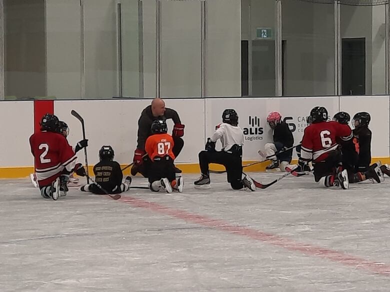 A group of hockey players kneeling around their coach on the ice.