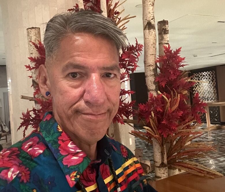 A man in a colourful shirt stands in a room.