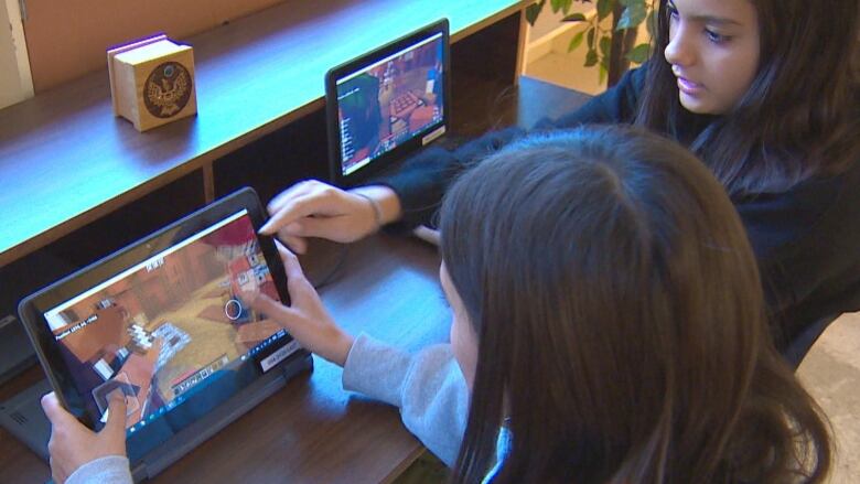 Two teenage girls play Minecraft video game on a laptop near a brown cedar wooden box with a bird carved on its lid.