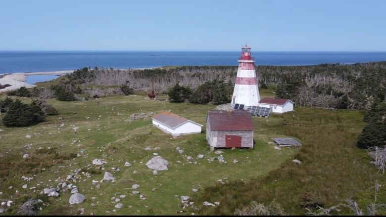 An aerial view of an octagonal wooden lighthouse with three smaller structures and a solar panel nearby. 