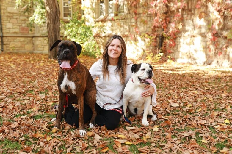 A woman with chest-length hair squats between her two dogs for a photo