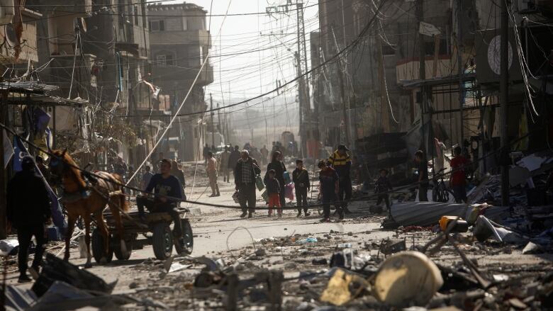 A wide view of a street with debris items strewn across between buildings with a number of people walking in the distance.