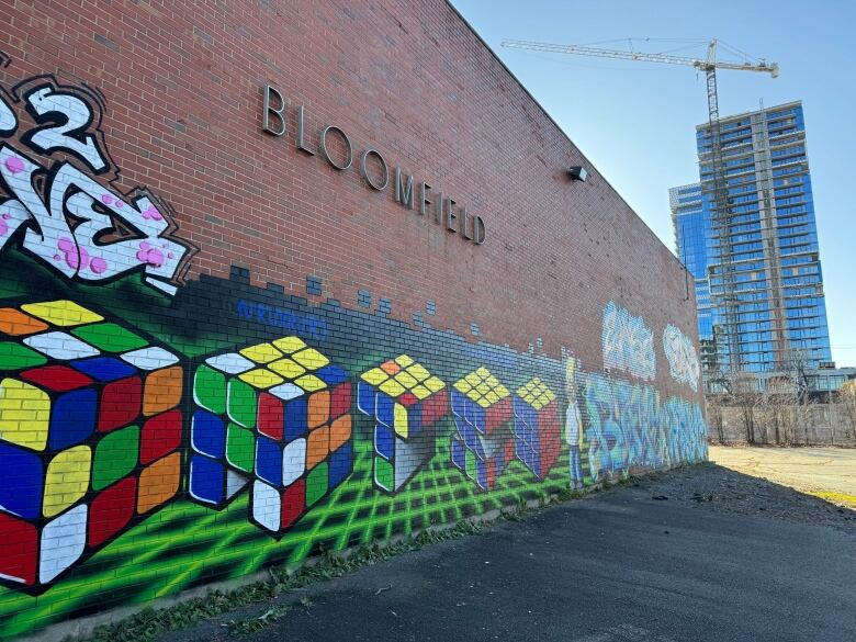 An exterior brick wall of the former Bloomfield School in Halifax, N.S., with graffiti painted over the lower half. A high-rise building and crane are seen in the background.