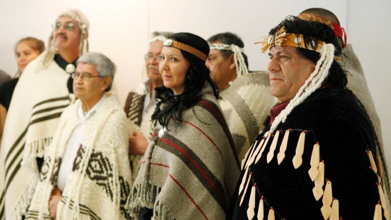 A group of people wearing Indigenous regalia are pictured from the side.