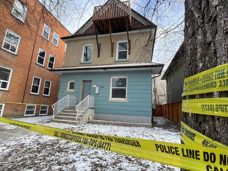 A home with blue and tan paneling is surrounded by police tape. 