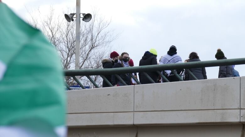 A group of people are shown standing on a bridge up above the camera.