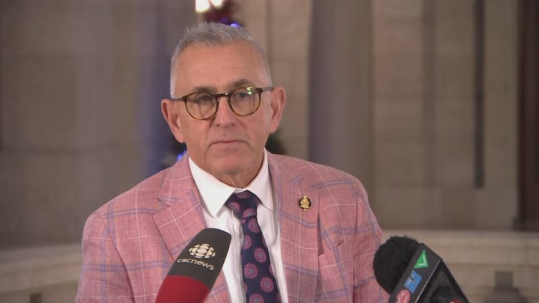 A man in a light red blazer stands behind a podium. 