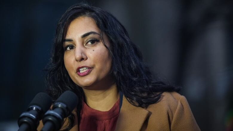 A South Asian woman speaks to a pair of mics.