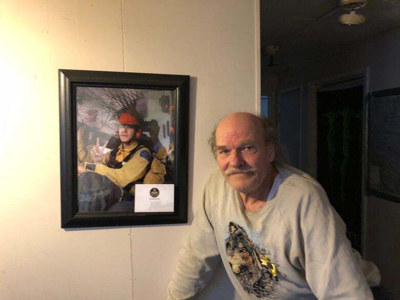 A man stands beside a photo on a wall. 