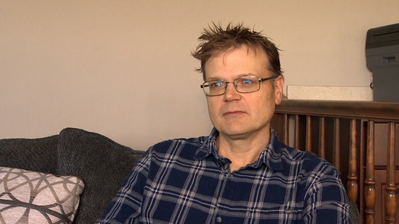 A man in a plaid shirt sits on a couch. 