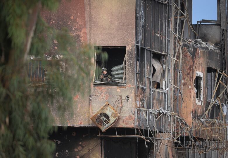 A soldier with a weapon is seen in the window of a damaged building.