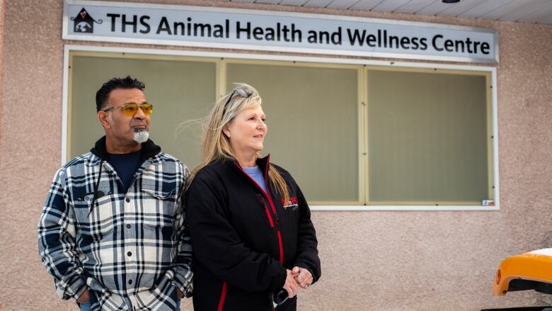 A man and woman stand outside a building that says THS Animal Health and Wellness Centre.