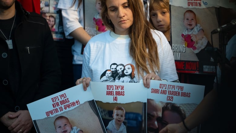 A woman holds up three placards with pictures of children, at what appears to be an outdoor demonstration.