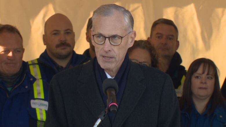 Old man with a side part wearing a black coat and glasses