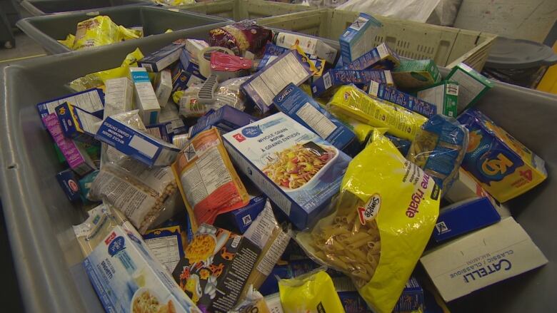 A big bin filled with food bank donations, including a single box of whole wheat pasta.