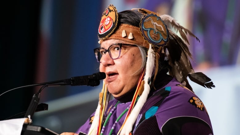 Woman in headdress speaks at a microphone and podium.