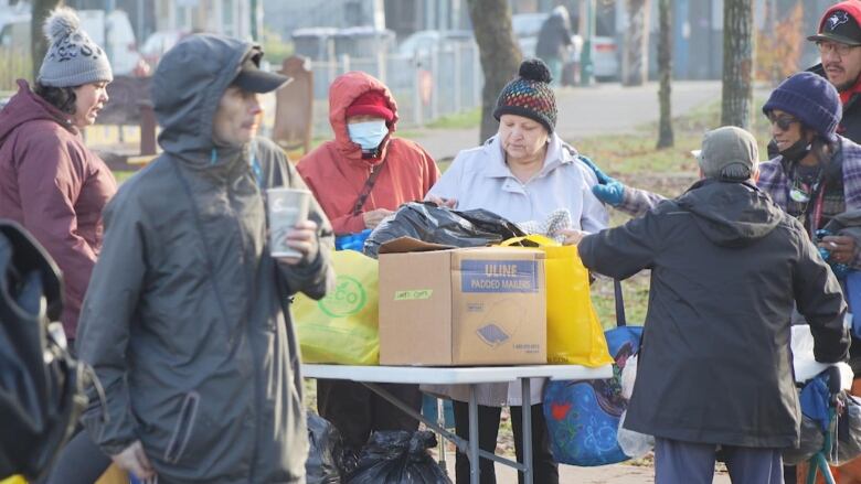 A group of people look through bags and boxes of clothing on a table outdoors.