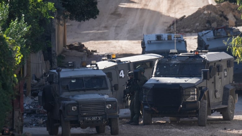 Several dark green military vehicles gathered on a dirt road.