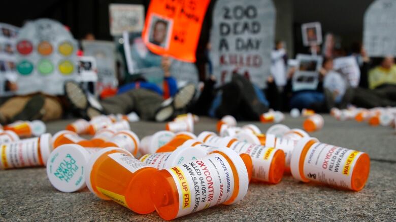 A number of pill bottles litter a pavement in front of signs commemorating those killed by prescription opioids.