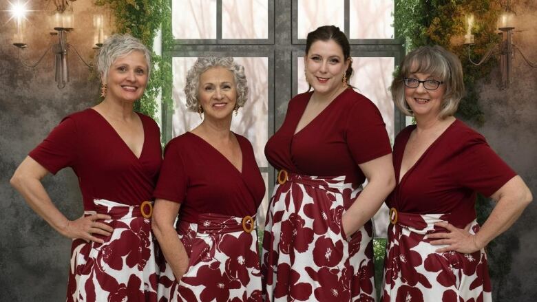 Four women dressed in matching burgundy tops and white and burgundy floral skirts pose for a smiling photo. 