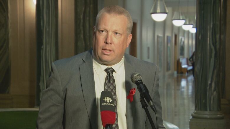 A man in a grey suit speaks, Saskatchewan Social Services Minister Gene Makowsky, speaks to reporters in front of microphones at the legislature.