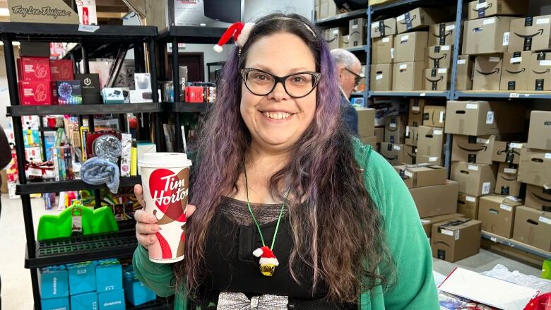 A smiling woman with long, curly hair dyed purple in some places holds up a ginormous cup of coffee. 