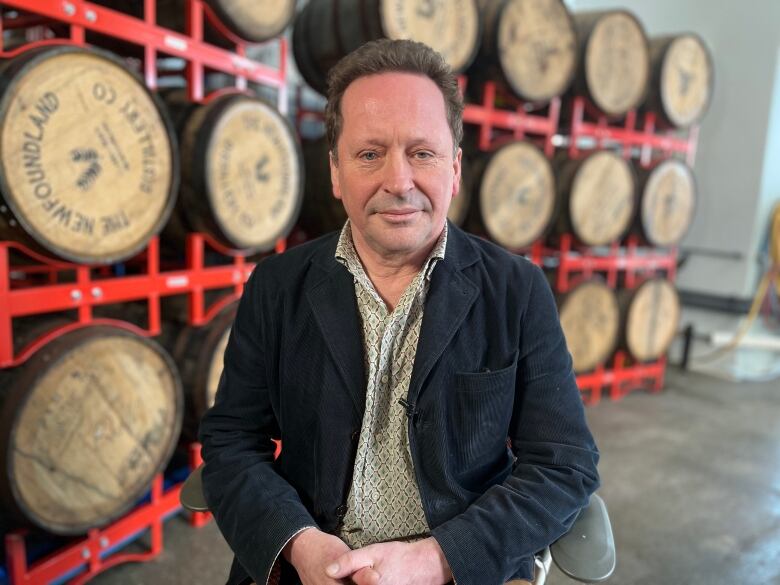 A man sits in a chair in front of shelves of barrels.