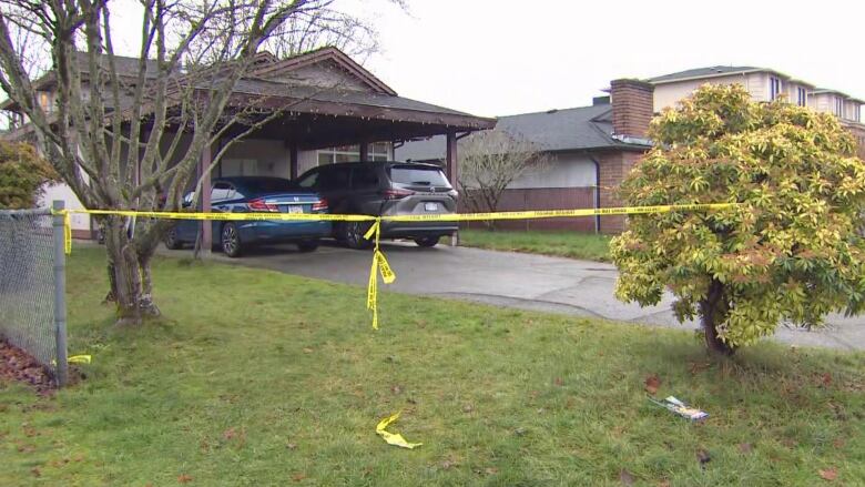 Yellow crime tape covers the lawn of a single-family home, with two cars.