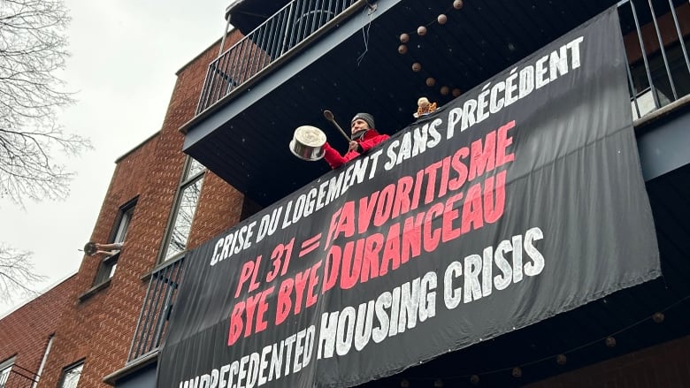 A person hangs a banner from a balcony.