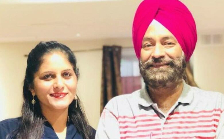 An Indian man and woman smile at the camera. The man is wearing a pink pagri (turban).