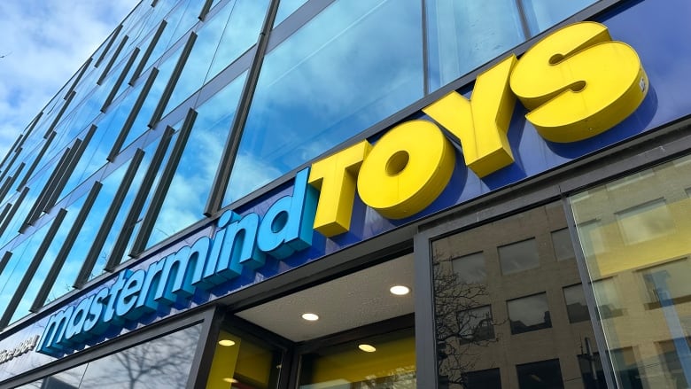 A blue and yellow sign affixed to a building says Mastermind Toys.