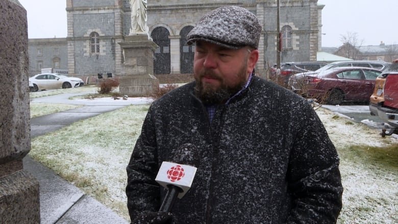 A person wearing a black jacket covered in falling snow stands in front of a large basilica.