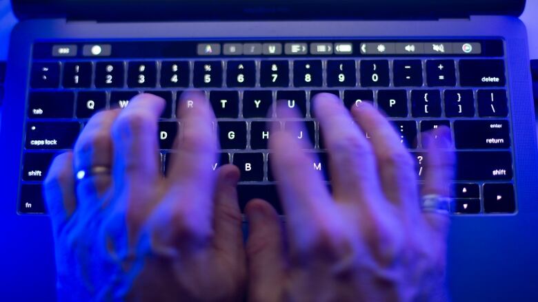 A person types at a laptop, with a blue light emitting from the screen.