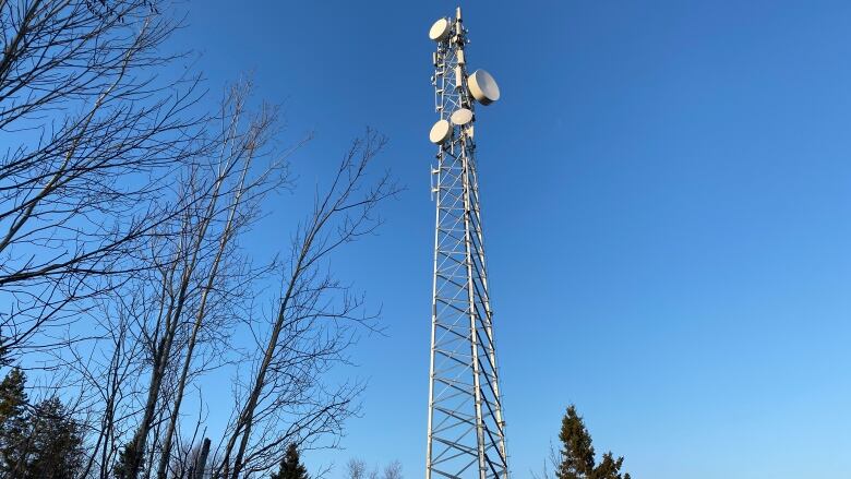 A tall silver tower with dishes on it against the blue background of sky