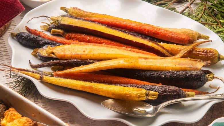 A white serving platter of roasted heirloom carrots on a wooden table set for a dinner. 