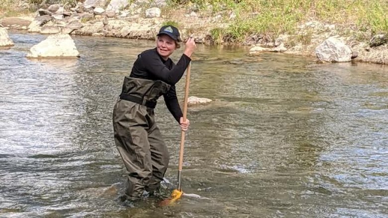 A woman pushes a stick into a body of water. 