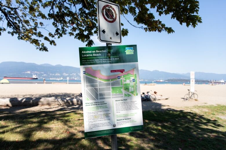 A signboard displays an area of a picturesque beach for an 'Alcohol on beaches pilot Locarno Beach', with text from the Vancouver Park Board laying out some guidelines.