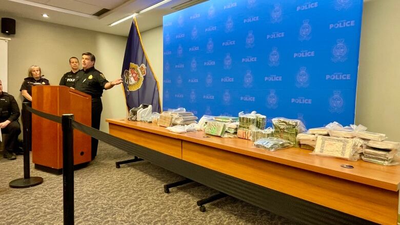 Police officers stand near a table covered with cash and drugs during a news conference.